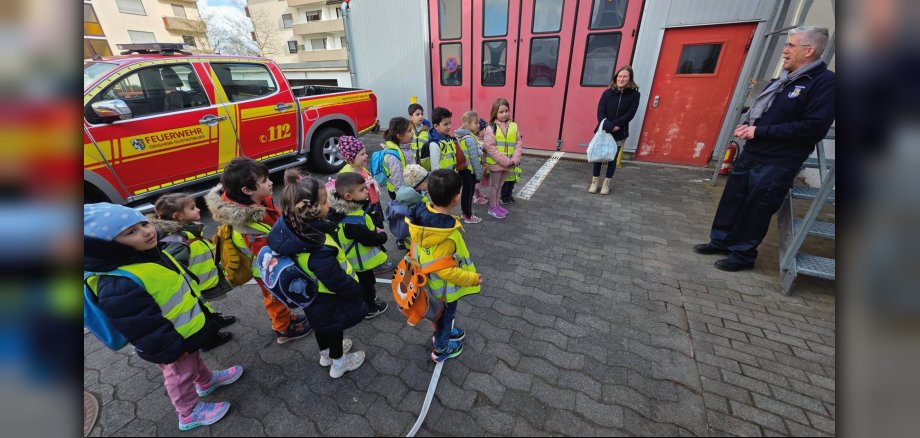 Frau Kollross (Erzieherin der Lukas-Gruppe) und Uwe Waldherr von der Feuerwehr Gustavsburg mit den gebannt lauschenden Kita-Kindern der Kita Lummerland