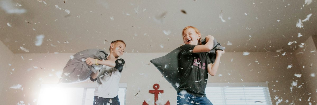 zwei Kinder auf einem Bett machen eine Kissenschlacht